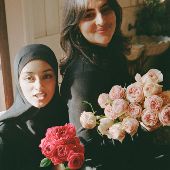 Two women smiling closely together, each holding a bouquet of pink and white roses.